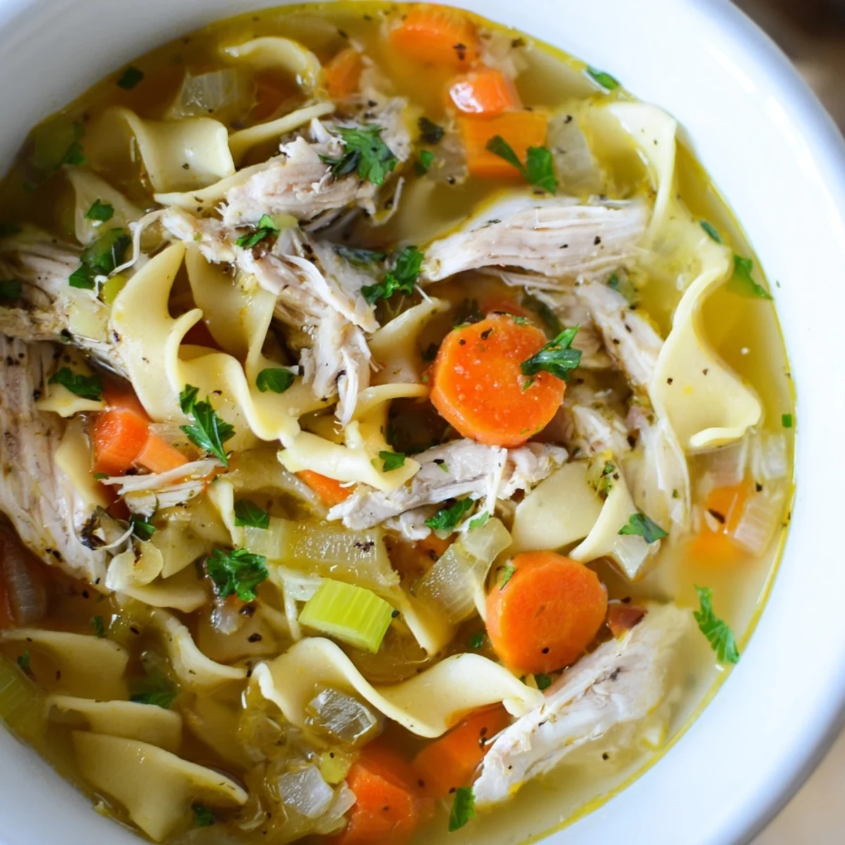 A close-up of Cozy Chicken Noodle Soup featuring golden egg noodles and fresh parsley garnish.