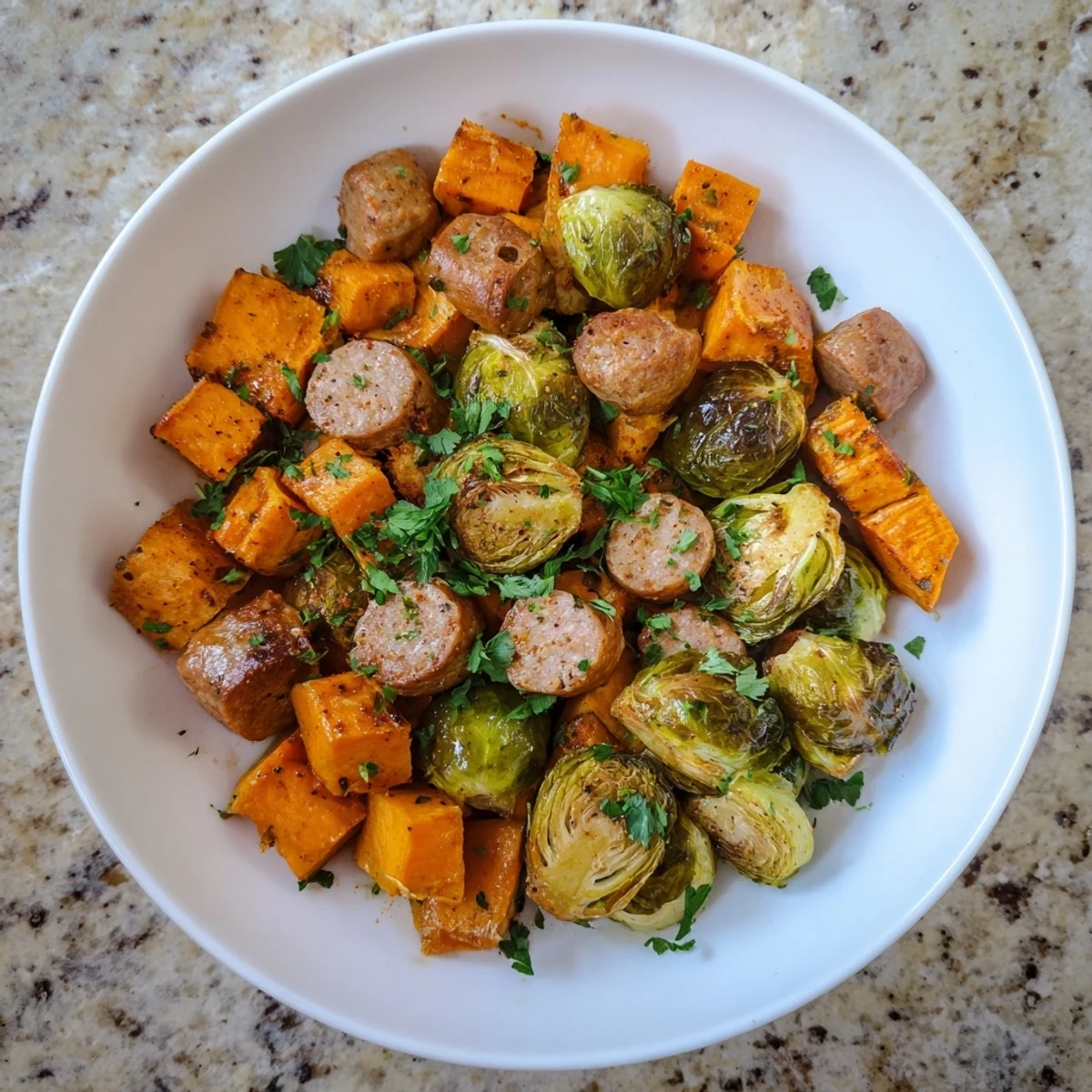 Golden-brown sheet pan sausage, sweet potato, and Brussels sprouts with a sprinkling of fresh parsley.