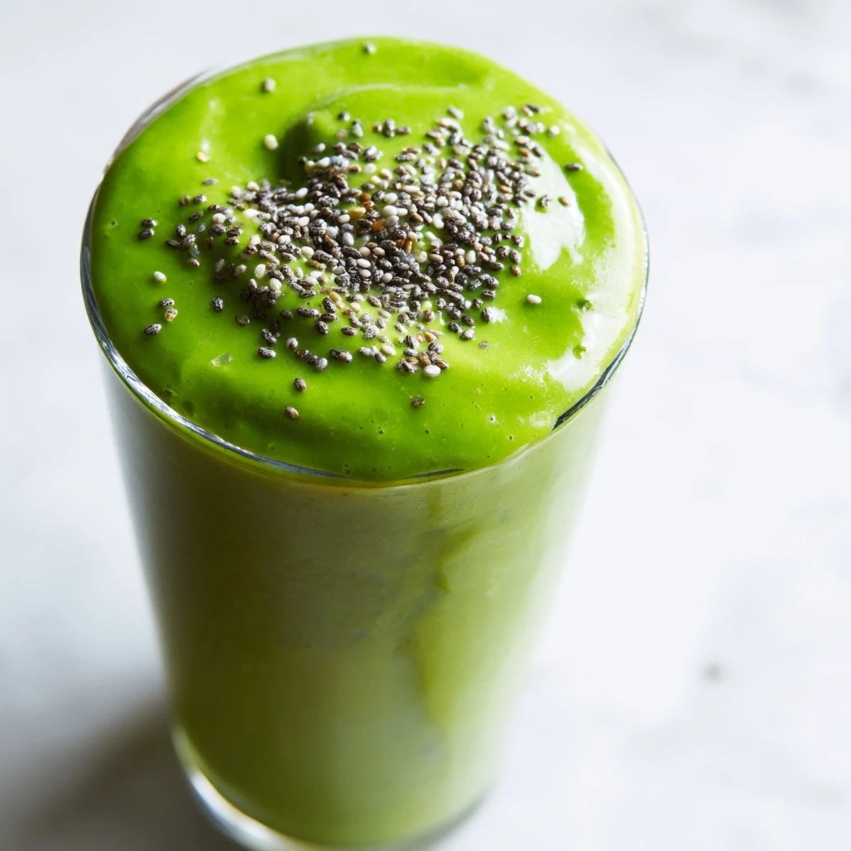 A close-up of a vibrant green spinach-hidden smoothie in a tall glass, garnished with fresh spinach leaves and a colorful straw for breakfast appeal. 