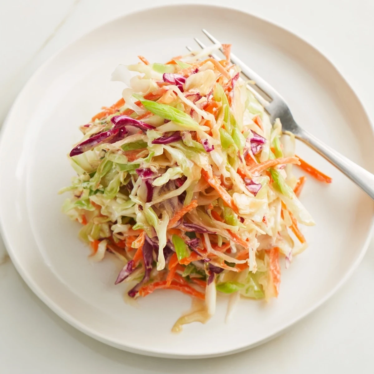 Crisp shredded green and red cabbage with grated carrots and green onions in a creamy Best Cabbage Coleslaw, served chilled in a white bowl.  