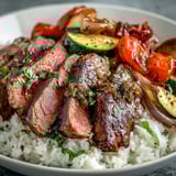 Golden roasted bell peppers and zucchini sit beside sliced steak on a bed of rice, drizzled with soy sauce for the Sheet Pan Steak and Veggie Bowl.