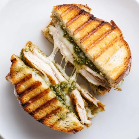 A close-up of grilled Chicken Pesto Panini with vibrant green basil pesto spread on warm ciabatta.