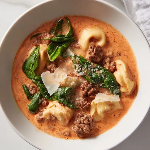 Close-up of Tuscan Tortellini Soup ladle over a bowl, highlighting rich red broth, tortellini, and fresh basil garnish.