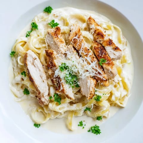 Sliced Cajun-seasoned chicken breast over fettuccine Alfredo, served warm with a velvety cream sauce and optional red pepper flakes.
