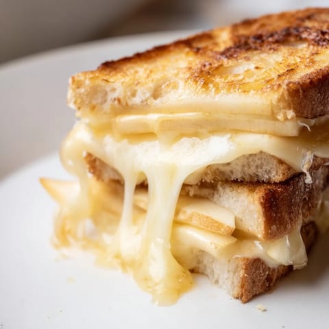 A close-up of the Smoked Gouda & Apple Grilled Cheese, highlighting its gooey cheese and buttery, toasted crust.