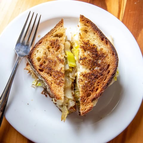 A close-up of Havarti & Caramelized Leek Grilled Cheese beside a bowl of tomato soup, perfect for a cozy lunch.  