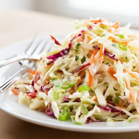 A fresh Best Cabbage Coleslaw tossed in a tangy dressing, perfect alongside grilled barbecue sandwiches at an outdoor summer picnic.  
