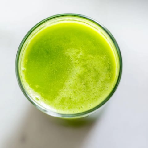 A tall serving of Cabbage and Kale Detox Juice over ice, showcasing bright emerald hues from kale, cabbage, and cucumber.  