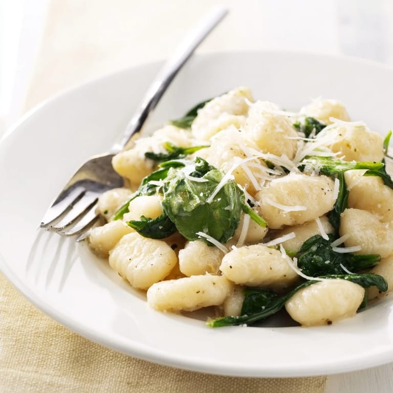 Close-up of Creamy Garlic Gnocchi in a skillet, garnished with fresh Parmesan and cracked black pepper.  