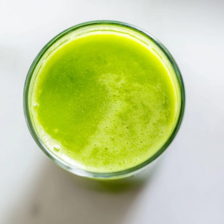 A tall serving of Cabbage and Kale Detox Juice over ice, showcasing bright emerald hues from kale, cabbage, and cucumber.  