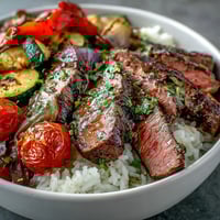 Juicy grilled steak and roasted vegetables from the Sheet Pan Steak and Veggie Bowl served over fluffy rice with lemon wedges.