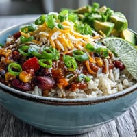Hearty Chili Bowl Base topped with shredded cheddar and sour cream over fluffy white rice for a comforting meal.