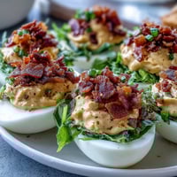BLT Deviled Eggs with Crispy Bacon Crumbles on a white platter, garnished with lettuce and tomatoes.